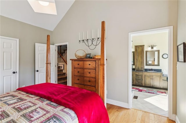 bedroom featuring light wood finished floors, baseboards, lofted ceiling with skylight, ensuite bath, and a sink