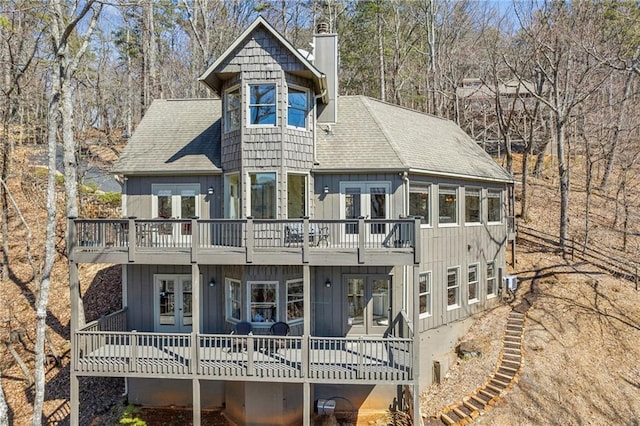 view of front of property with french doors, a chimney, a deck, and a shingled roof