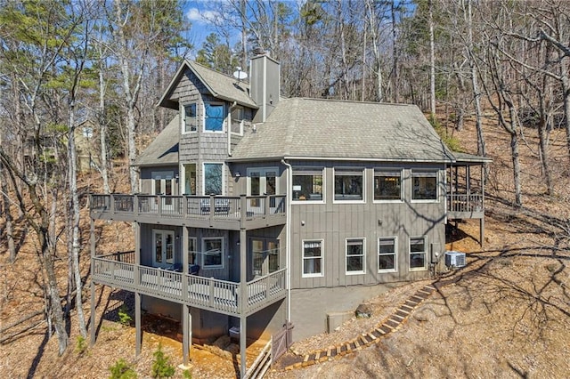 back of property with a wooden deck, central AC unit, a chimney, and roof with shingles