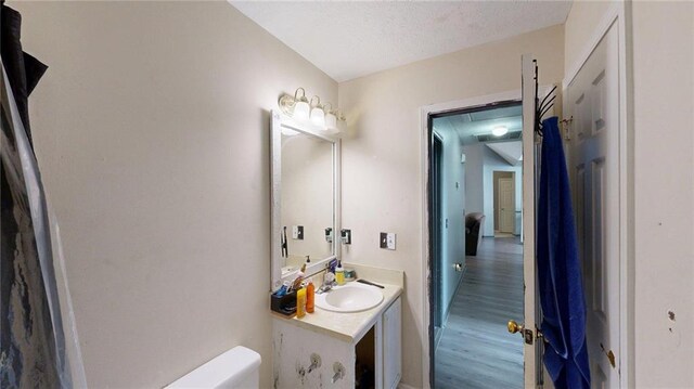 half bathroom featuring vanity, a textured ceiling, and wood finished floors