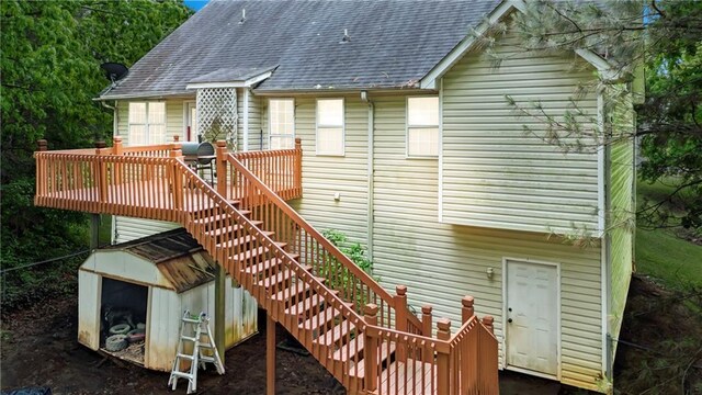 back of property with a wooden deck, stairway, an outdoor structure, a storage shed, and roof with shingles