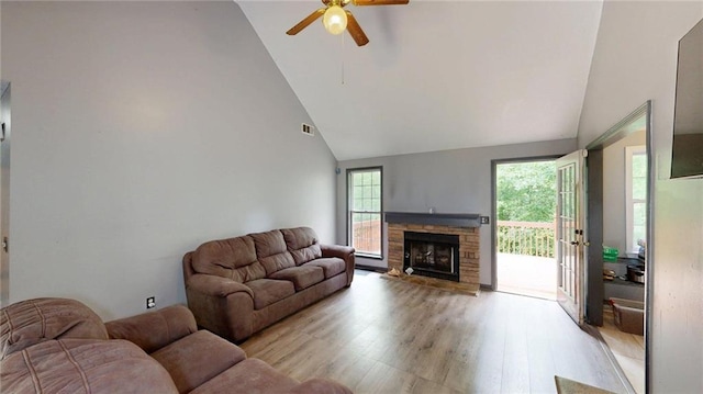living room with light wood-type flooring, ceiling fan, a fireplace, visible vents, and high vaulted ceiling