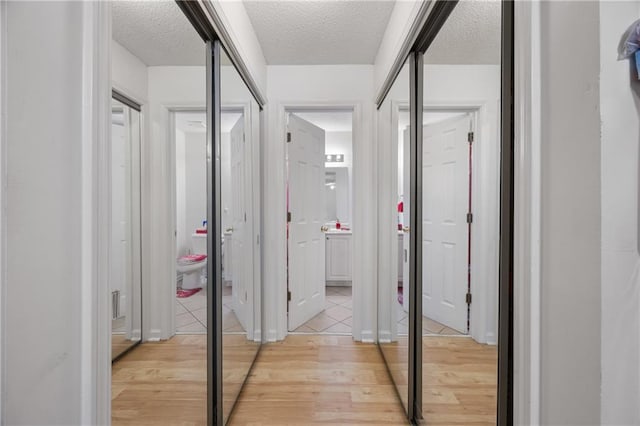 corridor with light wood-type flooring and a textured ceiling