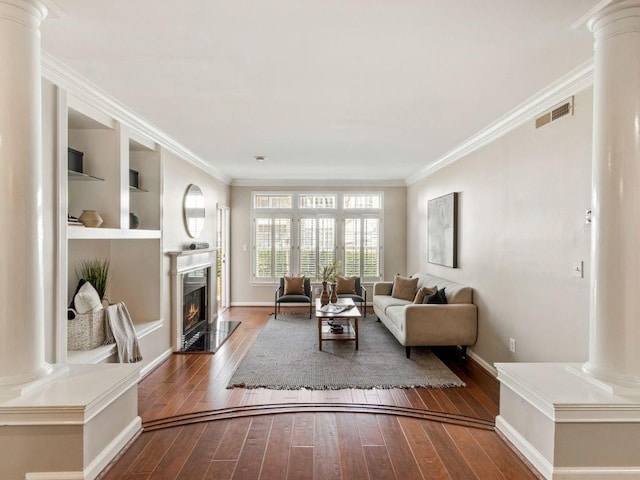 living area featuring visible vents, wood-type flooring, crown molding, and ornate columns