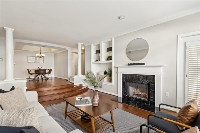 living area with a high end fireplace, built in shelves, ornamental molding, wood finished floors, and ornate columns