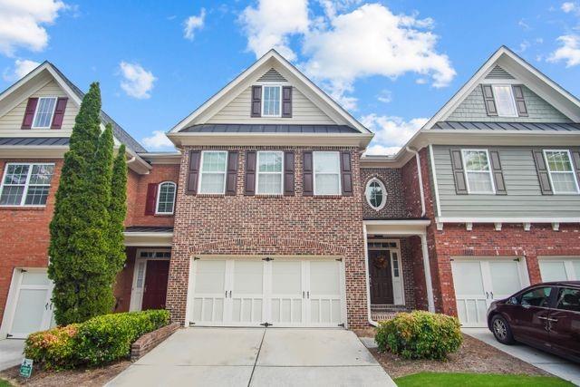 townhome / multi-family property featuring brick siding, metal roof, driveway, an attached garage, and a standing seam roof