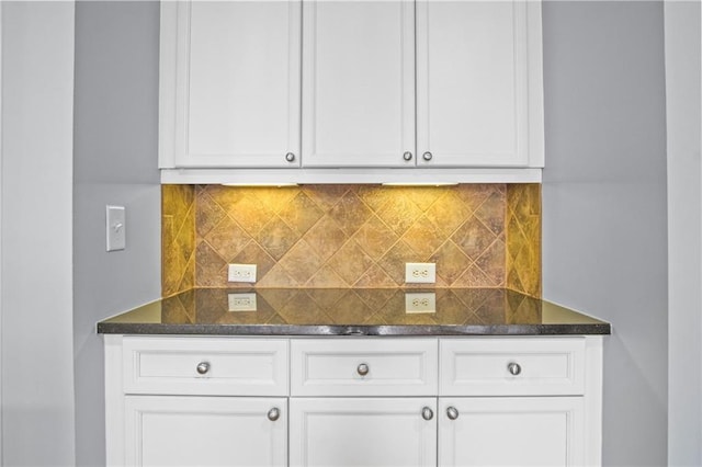 kitchen featuring dark stone counters, white cabinets, and backsplash