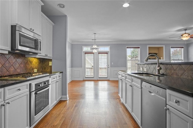 kitchen with light wood finished floors, a wainscoted wall, stainless steel appliances, a ceiling fan, and a sink