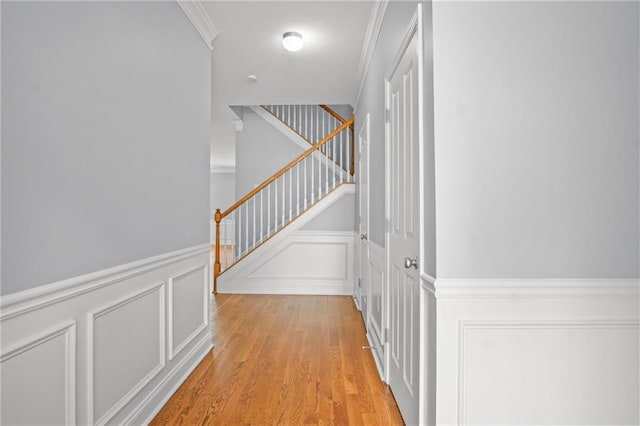 corridor with a decorative wall, stairway, crown molding, and light wood-style floors