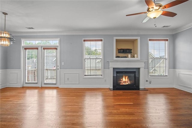 unfurnished living room featuring plenty of natural light, wood finished floors, a wainscoted wall, and a glass covered fireplace