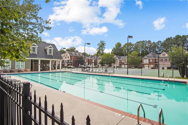 community pool with a patio area, fence, and a residential view