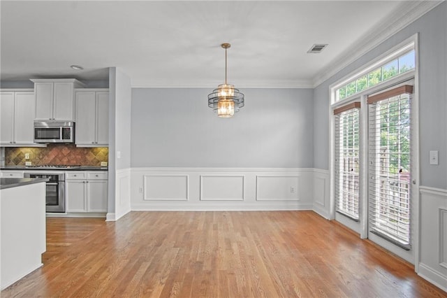 unfurnished dining area featuring light wood-type flooring, visible vents, an inviting chandelier, wainscoting, and crown molding