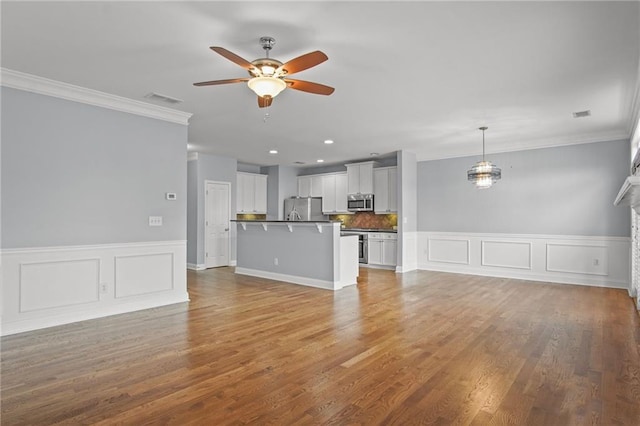 unfurnished living room with visible vents, crown molding, a ceiling fan, and wood finished floors