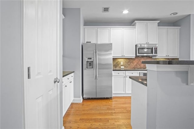 kitchen featuring dark countertops, visible vents, light wood-type flooring, appliances with stainless steel finishes, and white cabinets