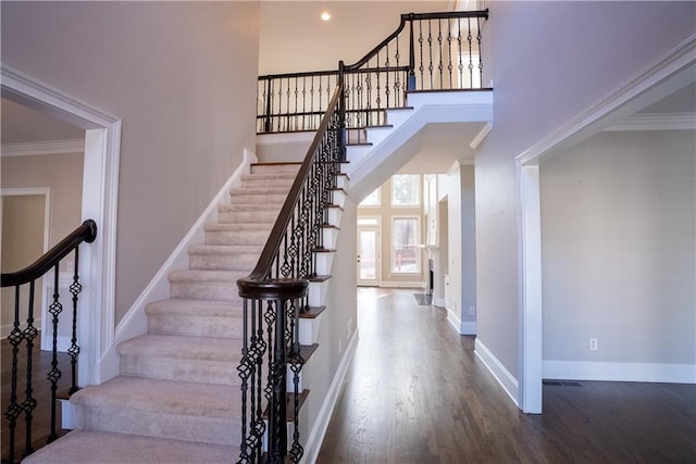 stairway featuring crown molding, a high ceiling, and hardwood / wood-style floors