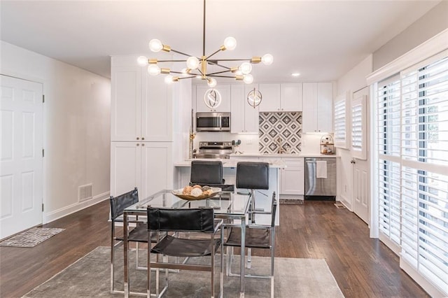 dining space featuring dark wood-type flooring, visible vents, baseboards, and a notable chandelier