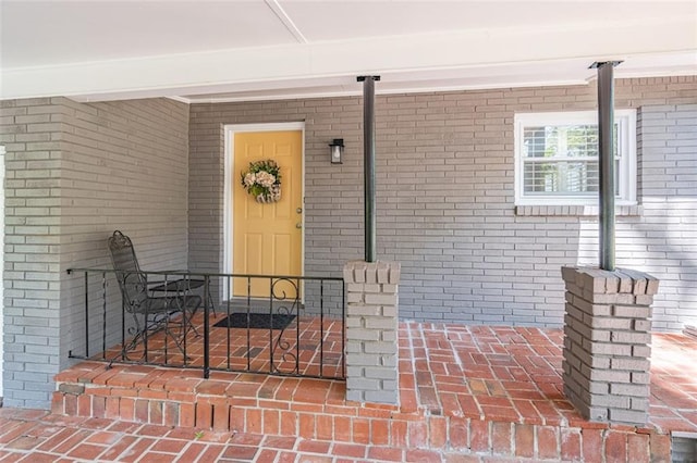 view of exterior entry with brick siding and covered porch