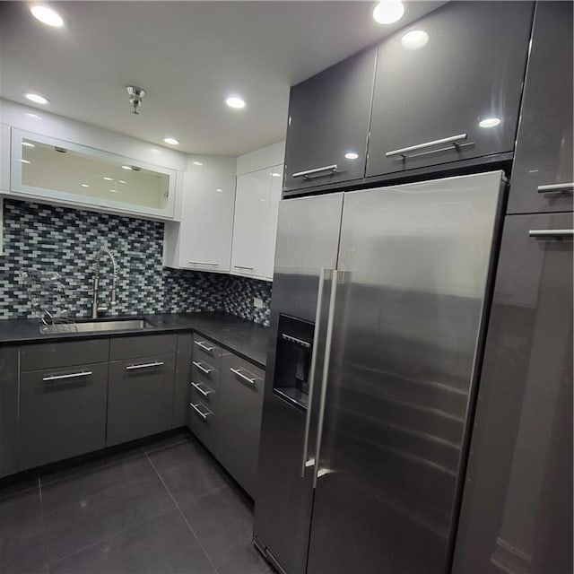 kitchen with a sink, stainless steel built in fridge, white cabinetry, dark countertops, and dark tile patterned flooring