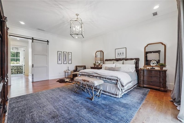 bedroom featuring ornamental molding, a barn door, hardwood / wood-style floors, and a chandelier