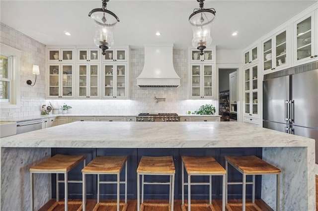 kitchen with custom exhaust hood, hanging light fixtures, a kitchen breakfast bar, and stainless steel appliances