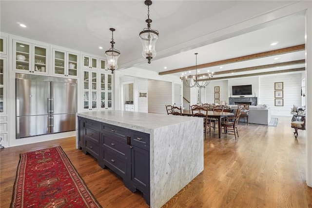 kitchen with built in refrigerator, an inviting chandelier, hardwood / wood-style floors, hanging light fixtures, and beamed ceiling