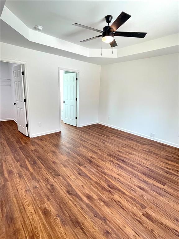 empty room with baseboards, a raised ceiling, ceiling fan, and wood finished floors