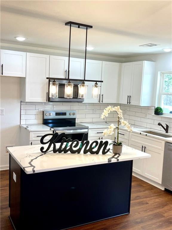 kitchen featuring a sink, dark wood-type flooring, appliances with stainless steel finishes, white cabinetry, and backsplash