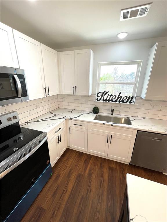 kitchen featuring visible vents, a sink, stainless steel appliances, light stone countertops, and dark wood-style flooring