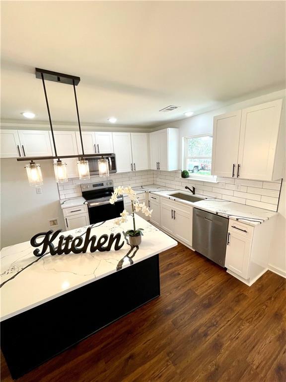 kitchen with dark wood-type flooring, decorative backsplash, stainless steel appliances, white cabinetry, and a sink