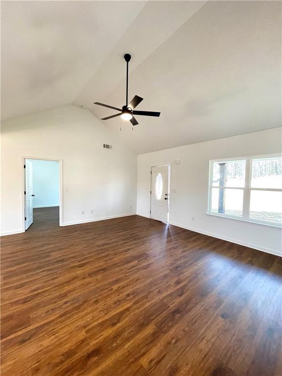 unfurnished living room featuring a ceiling fan, visible vents, baseboards, dark wood-style flooring, and vaulted ceiling