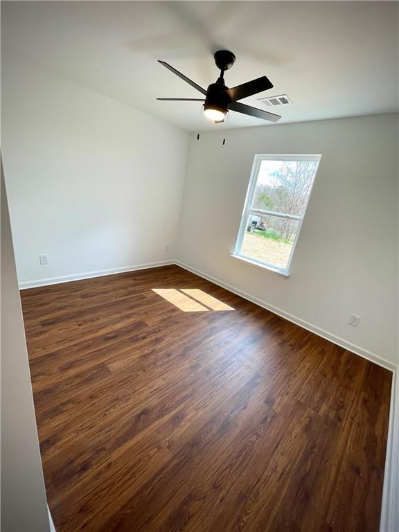 unfurnished room with visible vents, baseboards, dark wood-style floors, and a ceiling fan