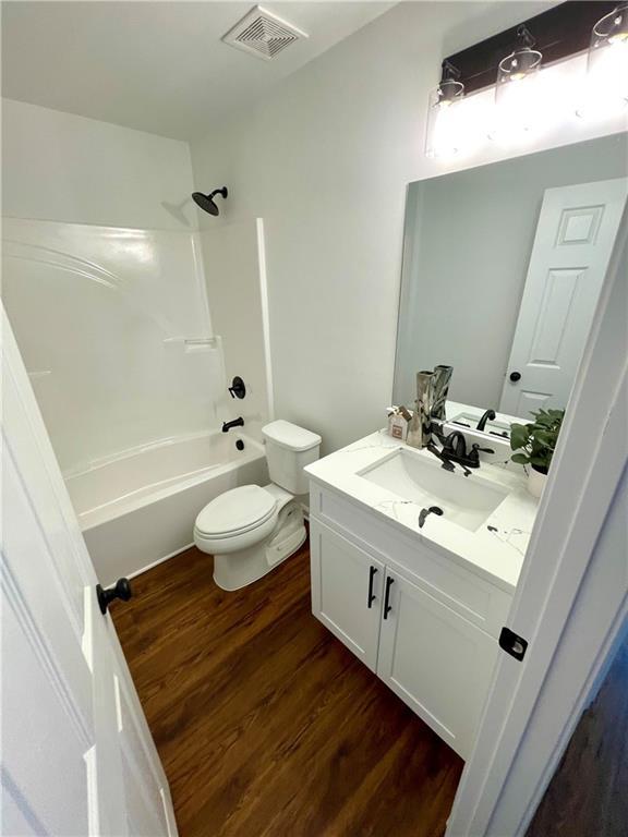 bathroom with visible vents, shower / washtub combination, toilet, wood finished floors, and vanity