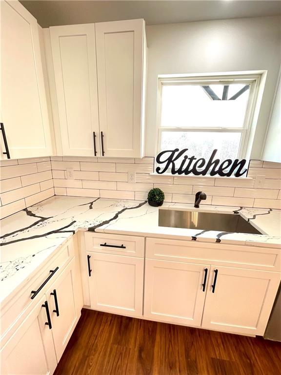 kitchen featuring backsplash, dark wood-type flooring, light stone counters, white cabinets, and a sink