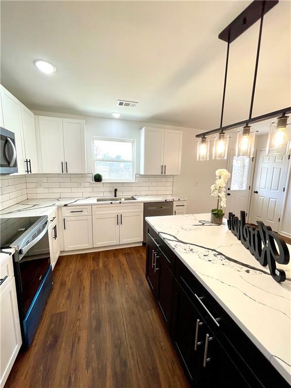 kitchen featuring stainless steel microwave, visible vents, decorative backsplash, electric range, and a sink