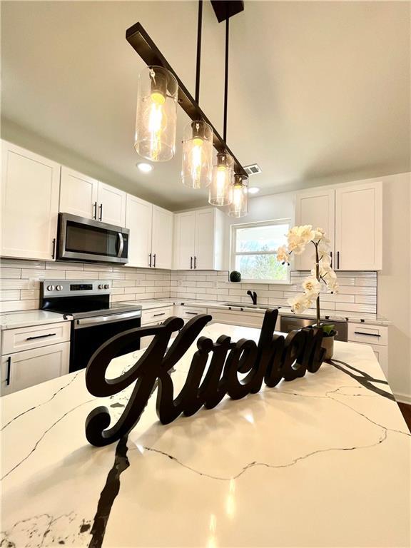 kitchen with light stone counters, stainless steel appliances, white cabinets, and decorative backsplash