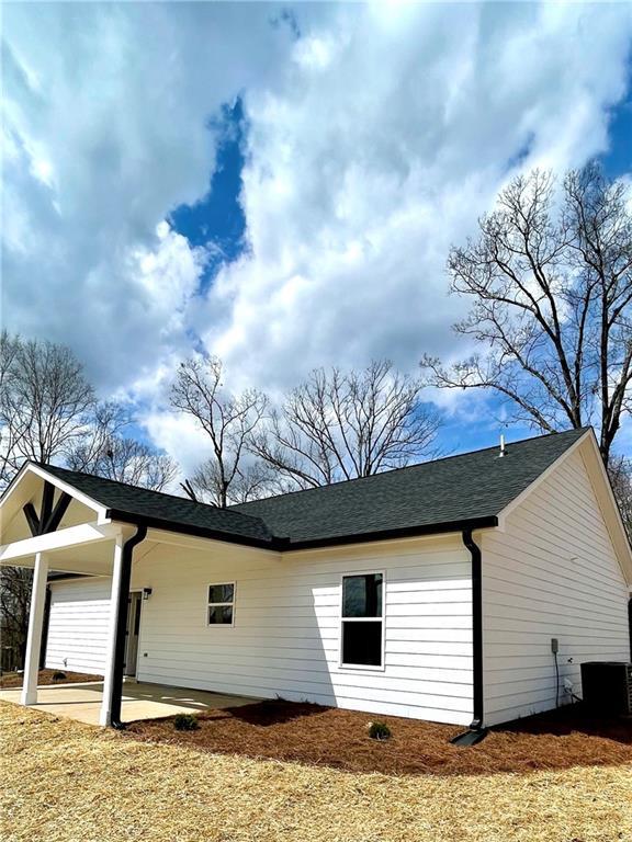 view of side of property with a patio area, central AC, and roof with shingles