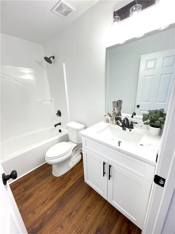 bathroom featuring visible vents, toilet, wood finished floors,  shower combination, and vanity