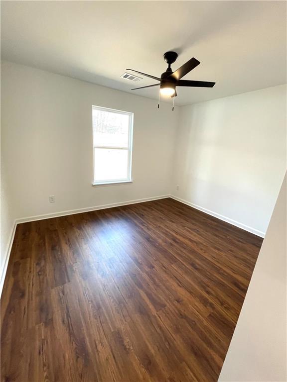 spare room featuring visible vents, baseboards, and dark wood-type flooring