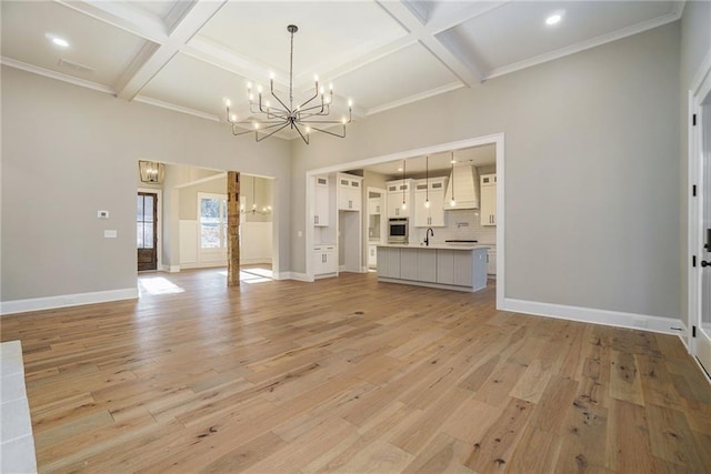 unfurnished living room with a chandelier, coffered ceiling, light wood-type flooring, beam ceiling, and baseboards