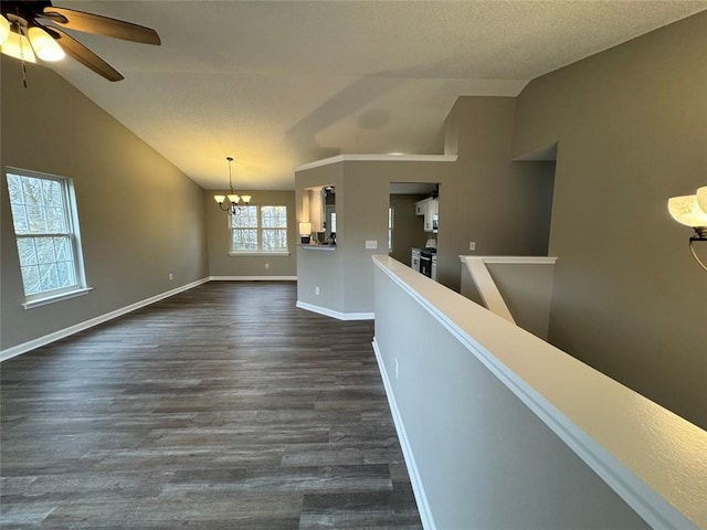 empty room with ceiling fan with notable chandelier, vaulted ceiling, plenty of natural light, and dark wood-type flooring