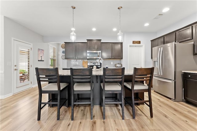6021 Harbour Mist Dr, Flowery Branch, GA 30542 - kitchen with appliances with stainless steel finishes, light wood finished floors, dark brown cabinets, tasteful backsplash, and a breakfast bar area