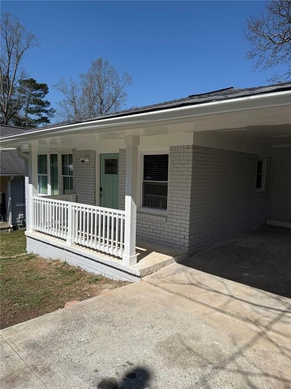 property entrance featuring an attached carport, covered porch, brick siding, and driveway