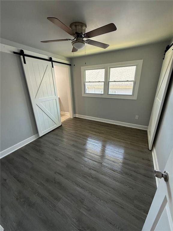 unfurnished bedroom with dark wood finished floors, a barn door, a ceiling fan, and baseboards