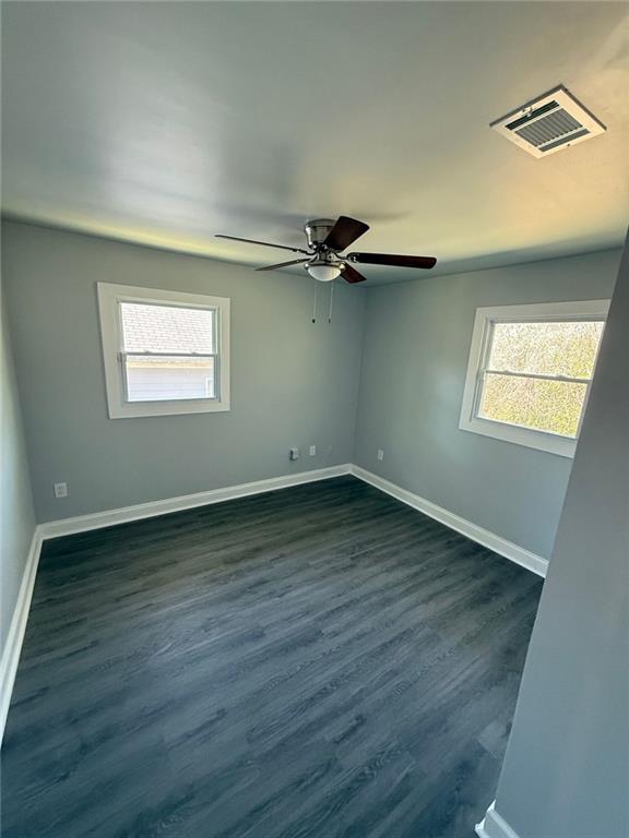 empty room with a ceiling fan, dark wood-style floors, baseboards, and visible vents