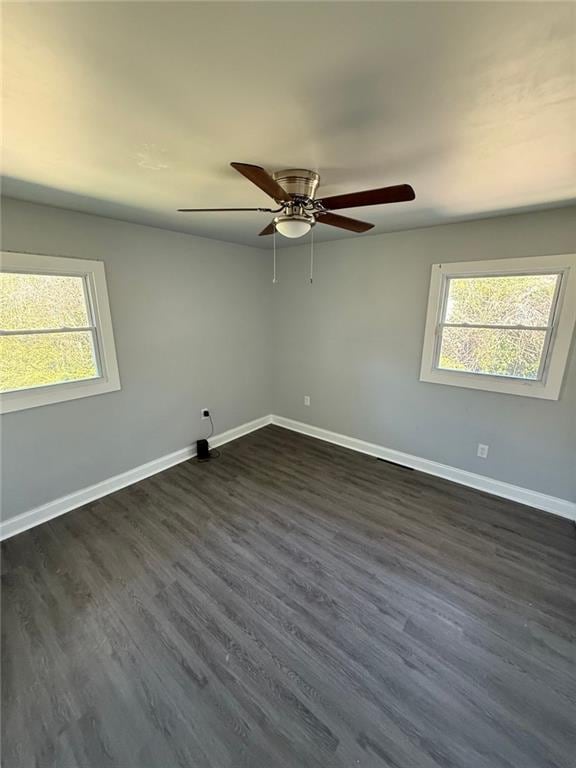 empty room featuring ceiling fan, baseboards, a healthy amount of sunlight, and dark wood-style floors