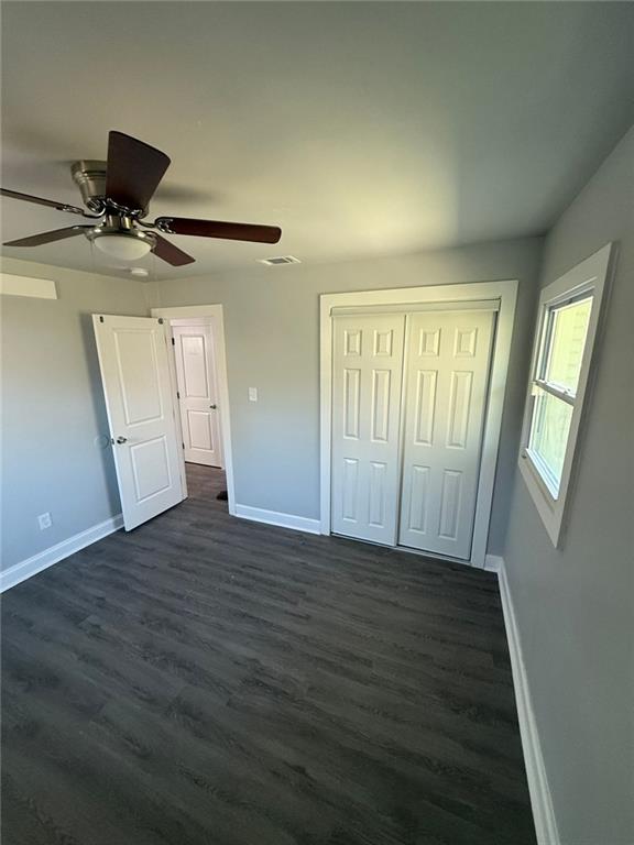 unfurnished bedroom featuring a closet, baseboards, dark wood-type flooring, and visible vents