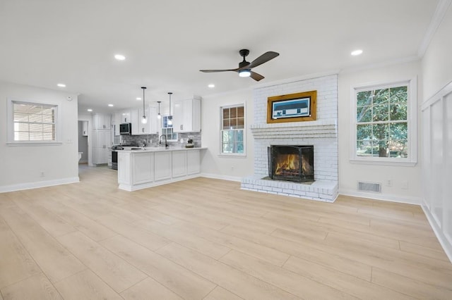 unfurnished living room with light wood-style flooring, visible vents, baseboards, ornamental molding, and a brick fireplace