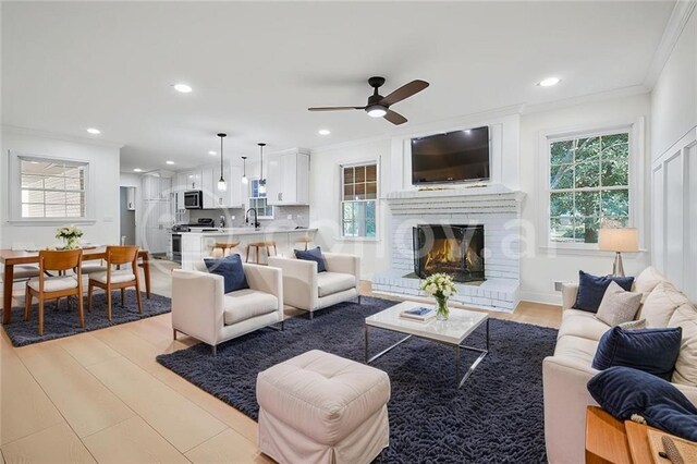 living room with a fireplace, ceiling fan, sink, and light wood-type flooring