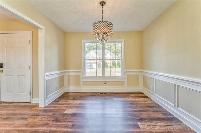 unfurnished dining area featuring dark wood-type flooring, an inviting chandelier, and a textured ceiling