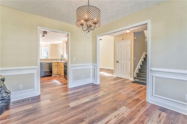 unfurnished dining area with hardwood / wood-style flooring, sink, a chandelier, and a textured ceiling